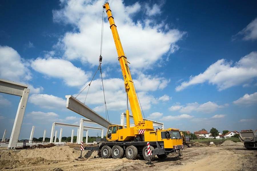Mobile telescopic crane lifting a precast beam at a bridge site