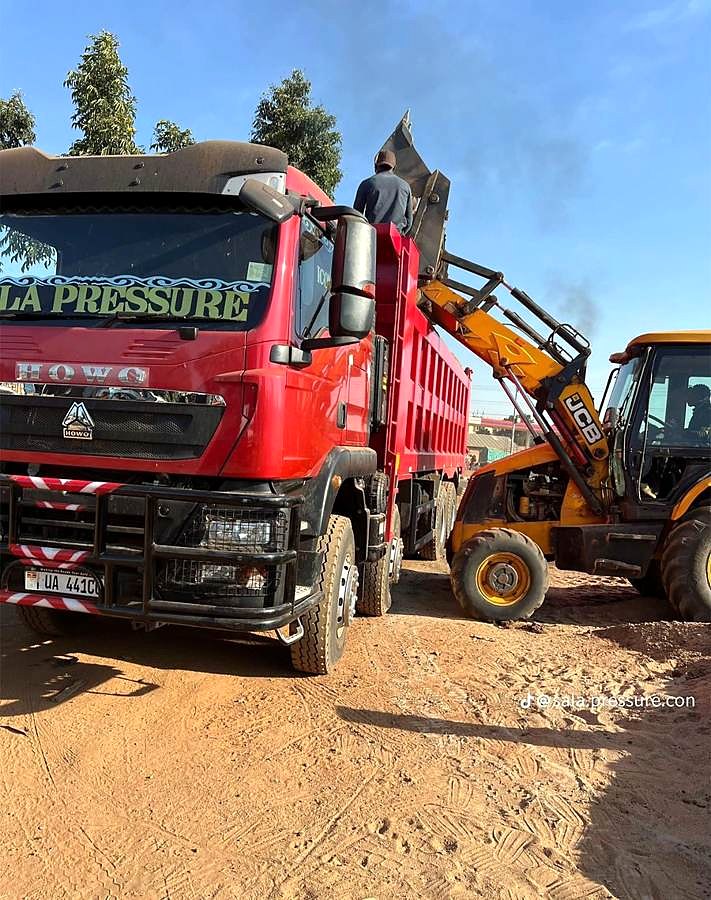 Backhoe loader loading a red tipper truck.